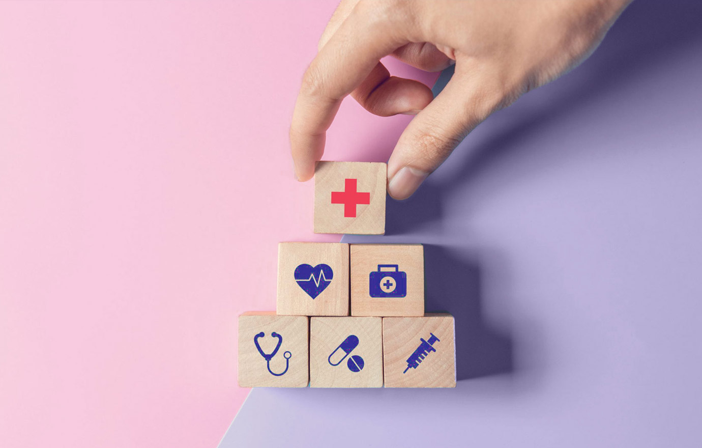 Dieses Bild zeigt eine Hand, die Bauklötze mit medizinischen Symbolen zu einer Pyramide stabelt